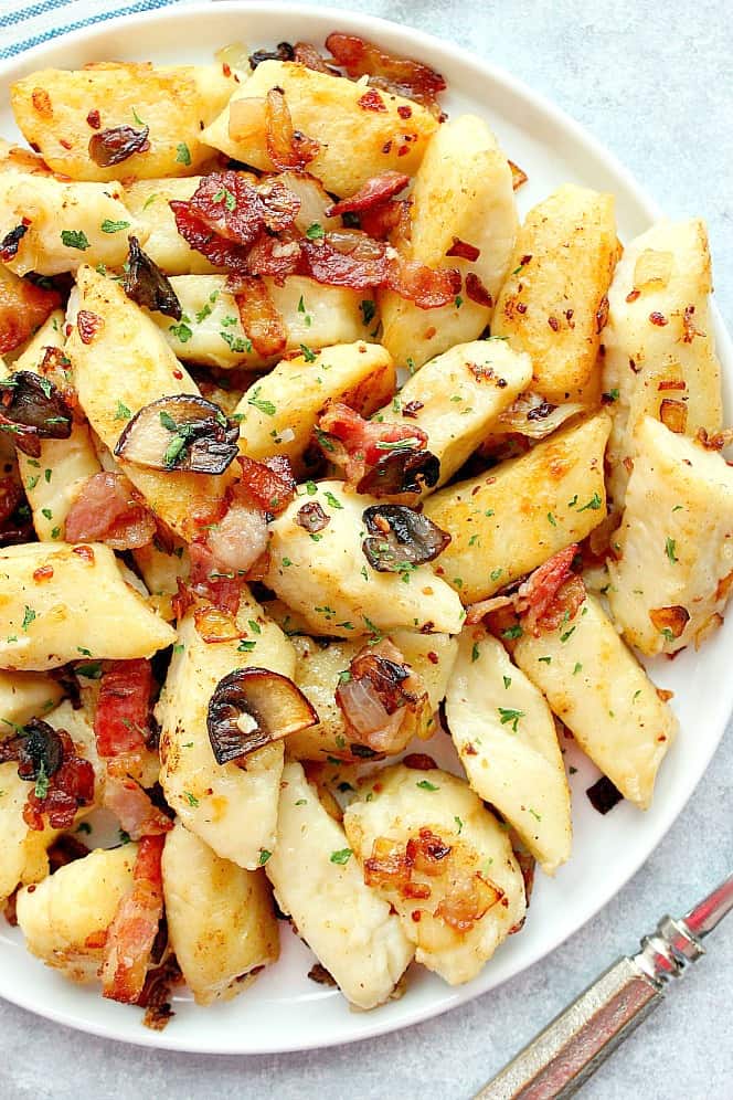 Overhead shot of Polish potato dumplings on white plate, with bacon and mushrooms.