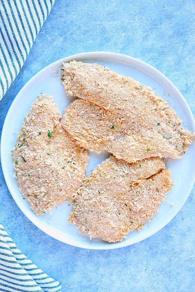 Overhead shot of three tilapia fillets, breaded on white plate.