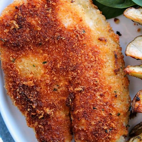 Crispy tilapia on a plate with fries and spinach.
