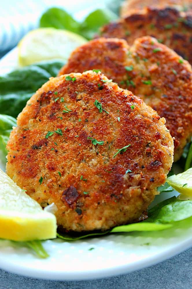 Side close up shot of 4 crispy fried tuna cakes on spinach leaves, with lemon slice on the side.