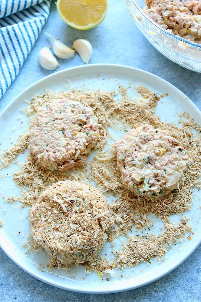 Overhead shot of three raw tuna cakes on a breadcrumb coating in shallow white dish.