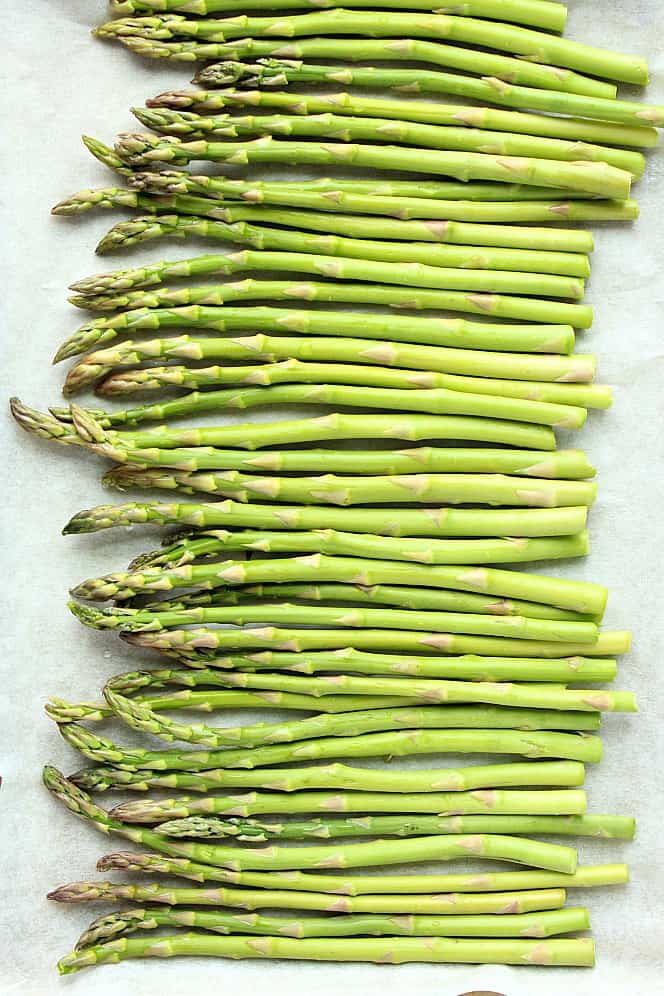 Overhead shot of fresh asparagus arranged on baking sheet with parchment paper.