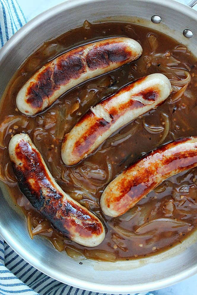 Overhead shot of sausage in onion gravy in pan.