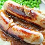 Sausage with onion gravy with green peas on a plate.