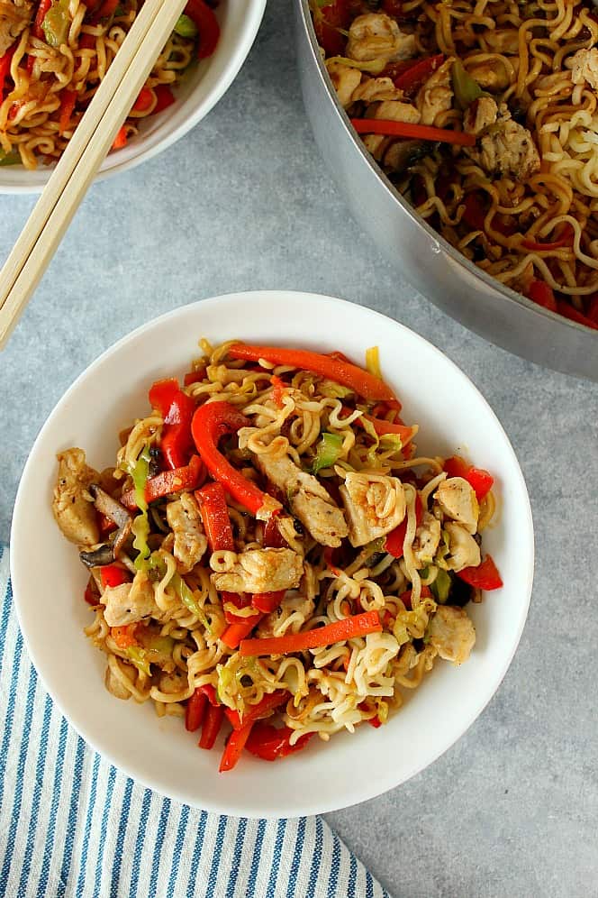 Chicken yakisoba in a white bowl, next to saucepan with more noodles.