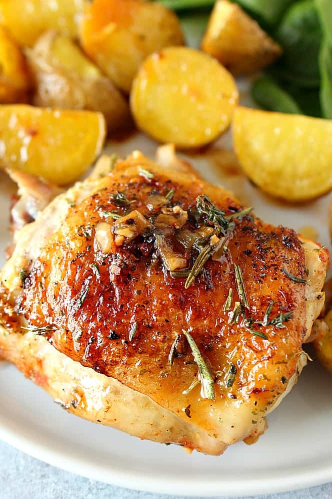 Close up shot of roasted chicken thigh on plate with baby potatoes on the side.