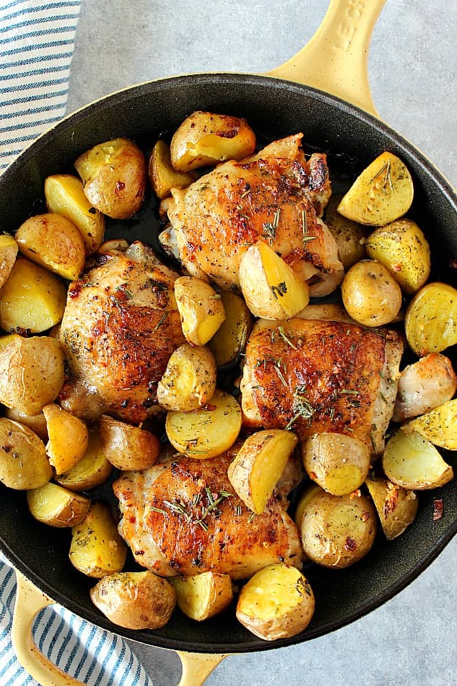 Overhead shot of garlic and herb chicken thighs with potatoes in skillet.