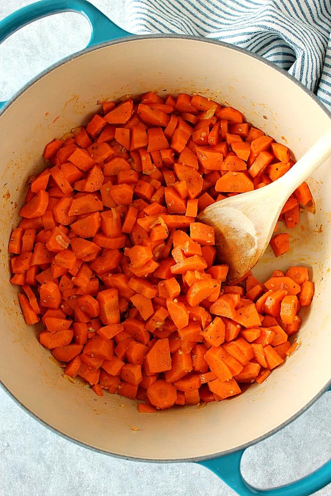 Dutch oven with chopped carrots inside, wooden spoon on the right.
