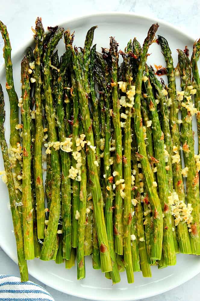 Overhead shot of roasted garlic Parmesan asparagus on white round plate.