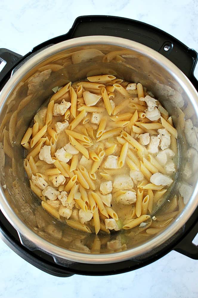 Overhead shot of chicken pieces and penne pasta in water in the Instant Pot.