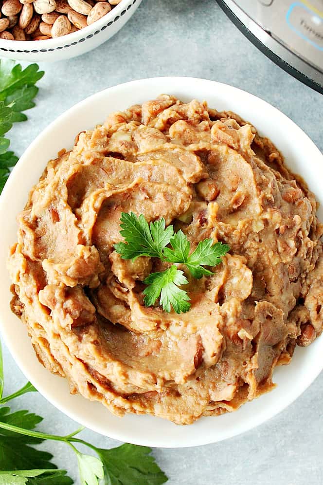 Overhead shot of refried beans in white bowl, with cilantro leave on top.