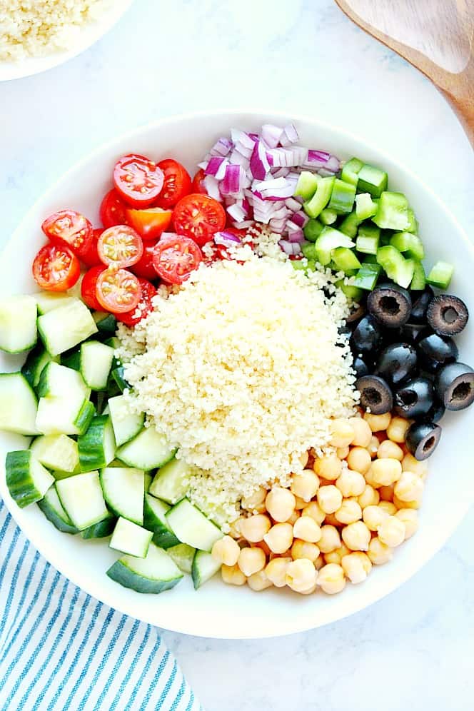 Overhead shot of ingredients for couscous salad, arranges in white bowl.