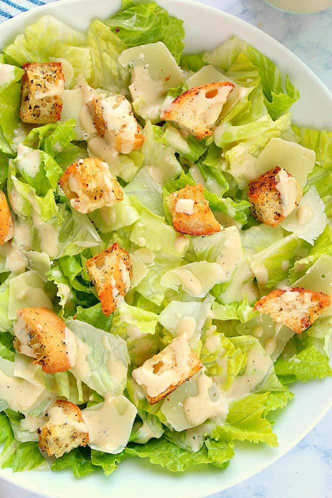 Close up shot of chopped Romaine lettuce, croutons, shaved Parmesan and dressing.