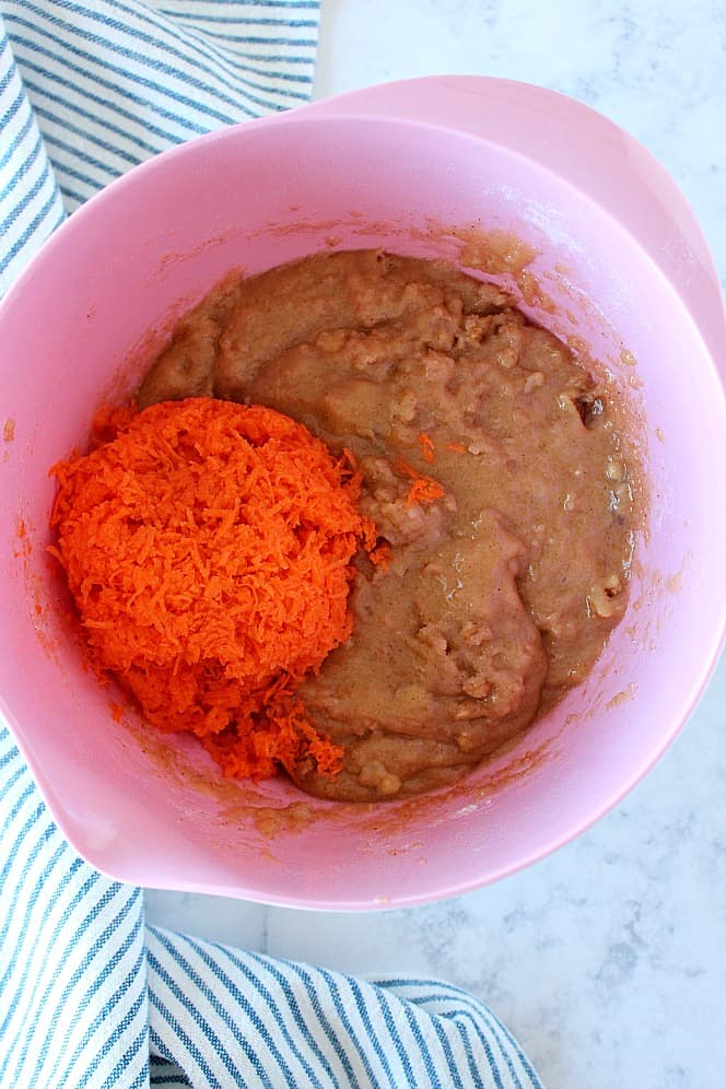 Overhead shot of carrot cake batter with shredded carrots in pink bowl.