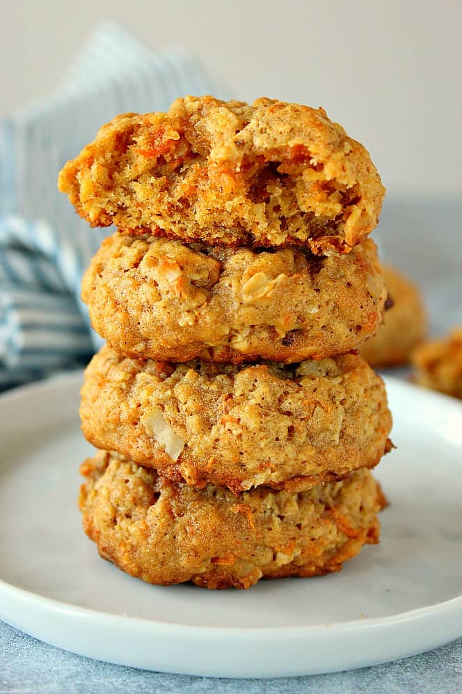 Side shot of four oatmeal carrot cookies stacked up on each other on white small plate.