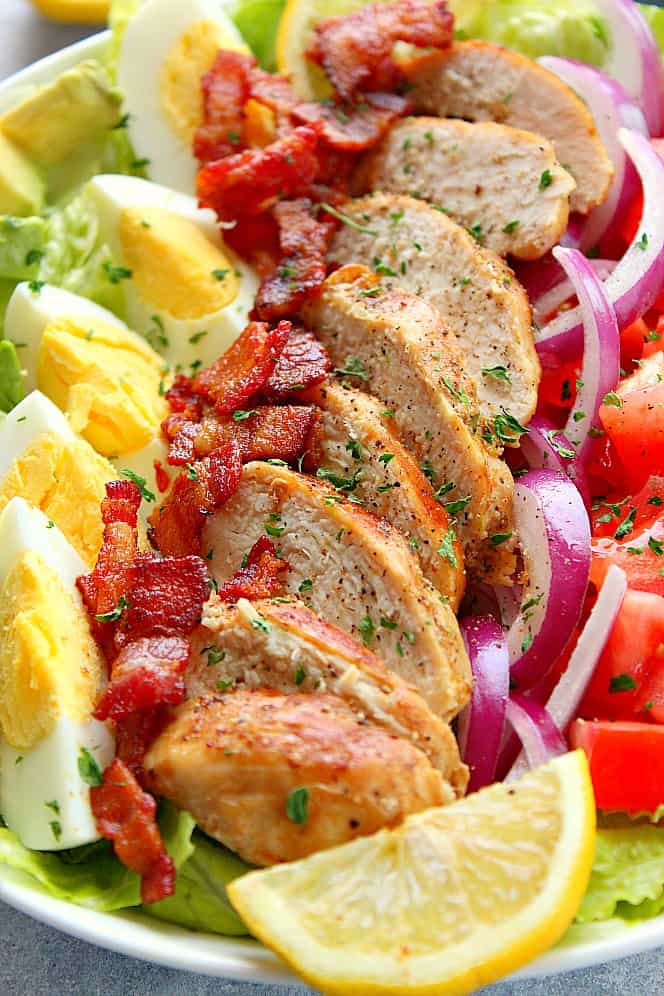 Side shot of chicken Cobb salad with bacon, eggs, onion and tomatoes.