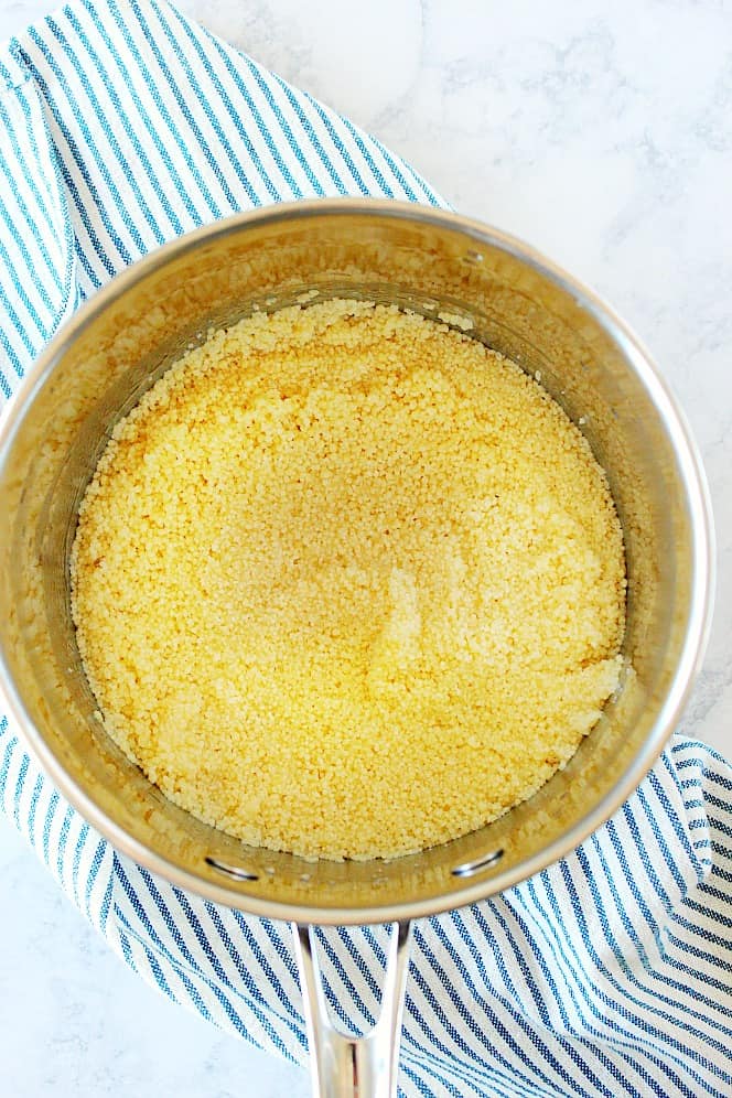 Overhead shot of couscous in water in a stainless steel pot.