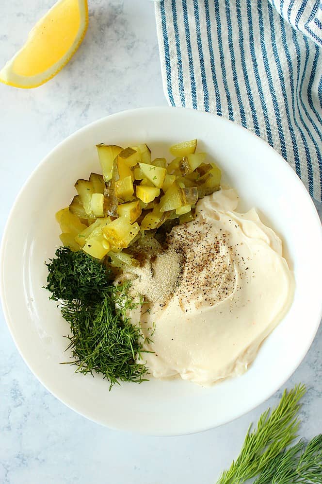 Overhead shot of mayo, pickles, dill, salt, pepper in white bowl.