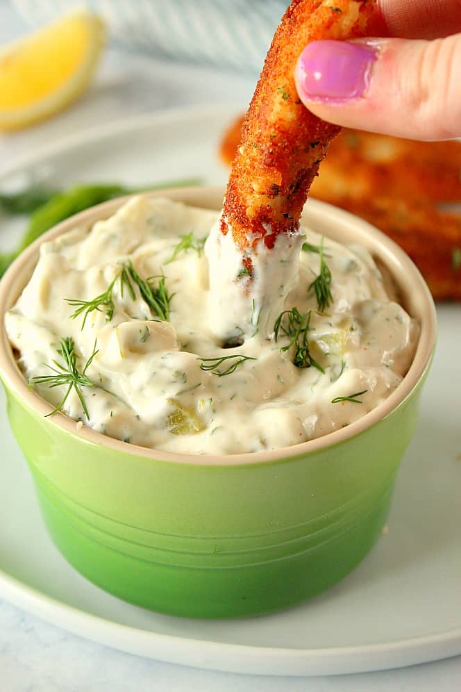 Side shot of golden fish stick dipped in homemade tartar sauce.