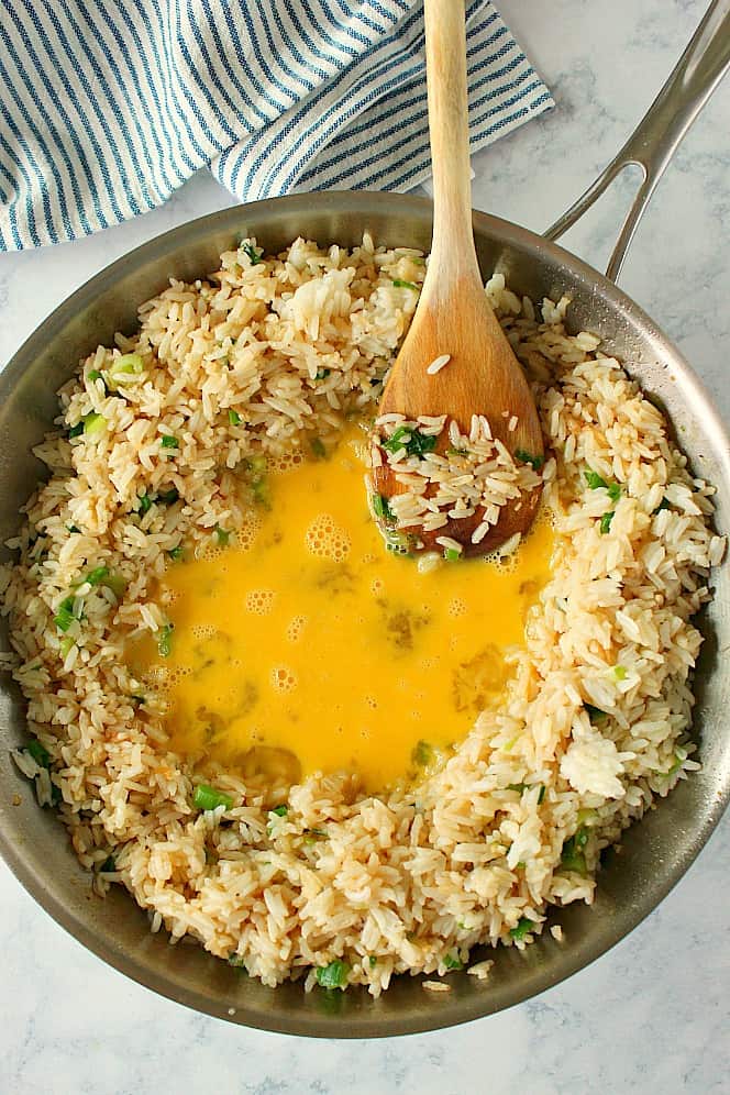Overhead shot of rice in skillet, with beaten eggs in the center of the pan.