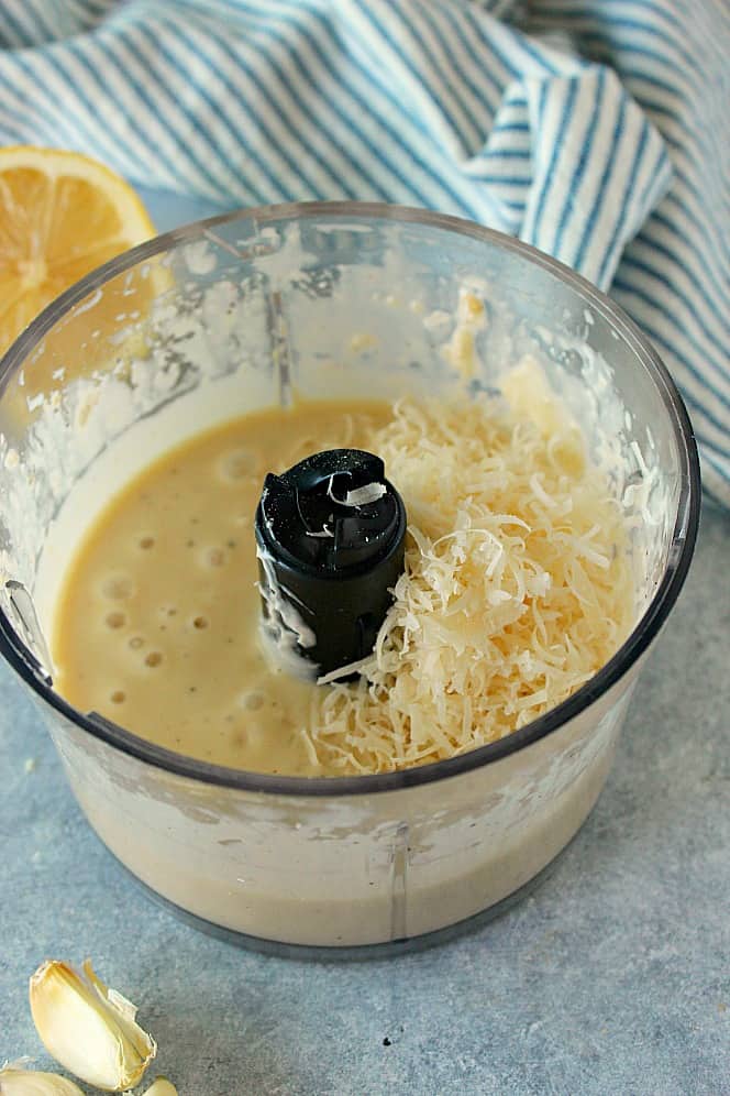 Side shot of Caesar dressing in mini food processor with grated Parmesan cheese added.