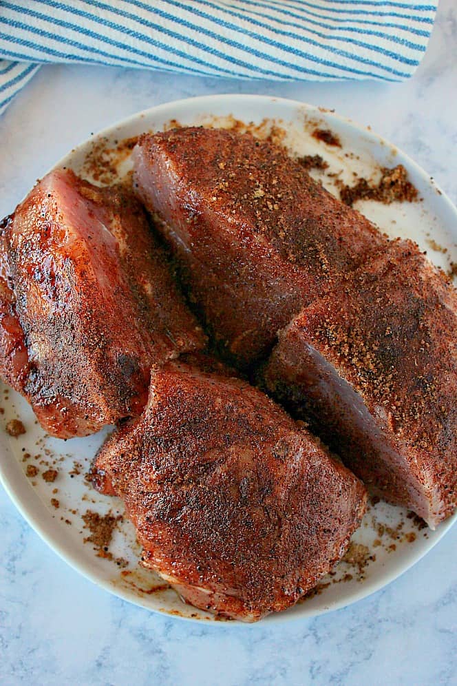 Pork roast cut into 4 pieces, with rub, on white plate.