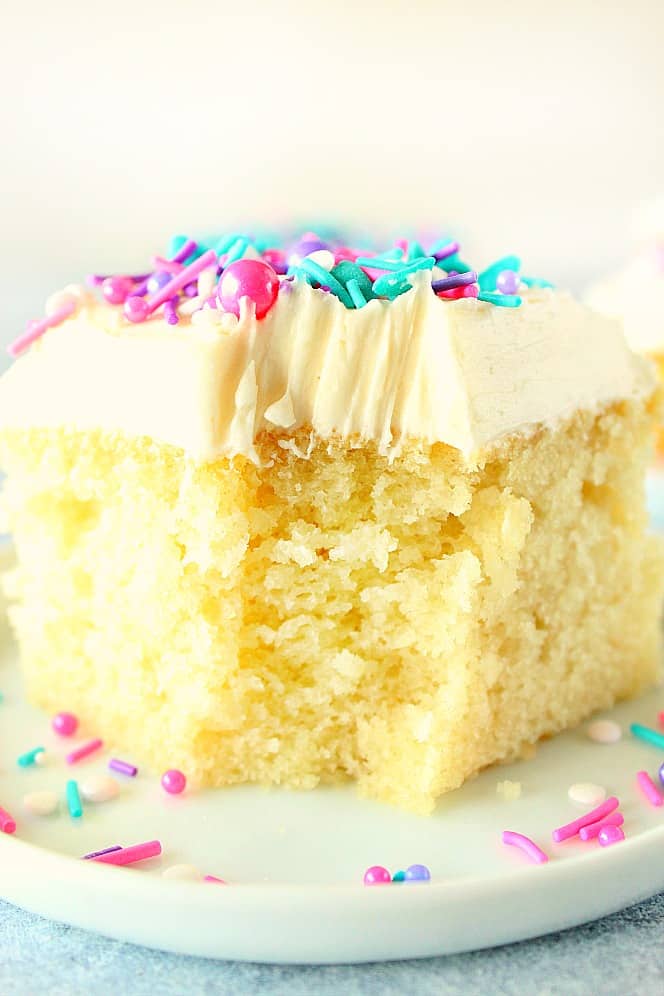 Close up shot of a piece of vanilla cake with frosting, one bite missing in front.