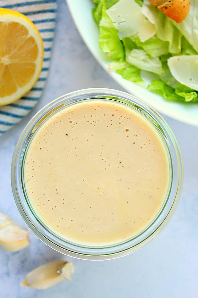 Overhead shot of Caesar dressing in jar, next to salad in bowl.