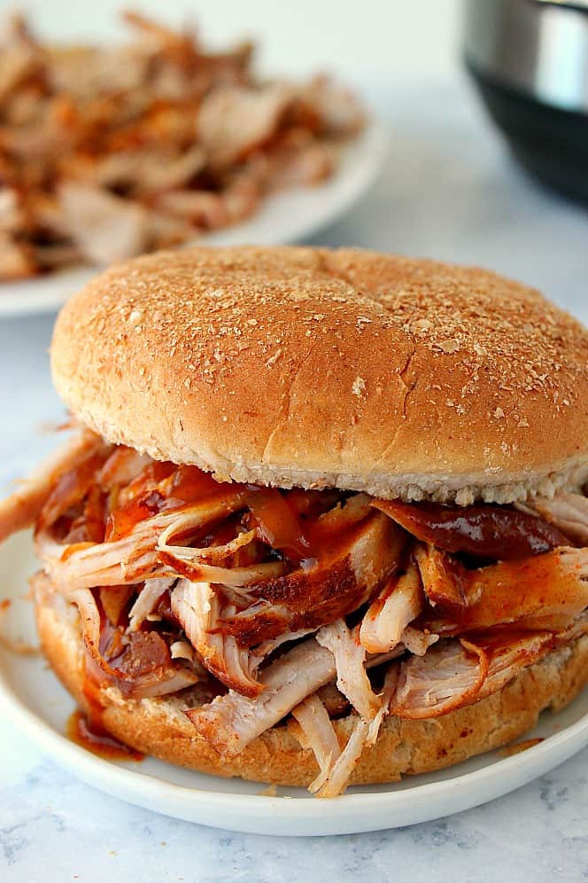 Side shot of pulled pork in bun, with Instant Pot in the background.