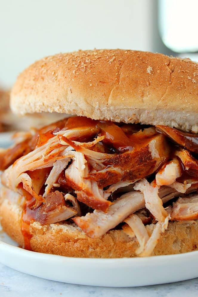 Pulled pork with BBQ sauce in a bun on a white dinner plate.