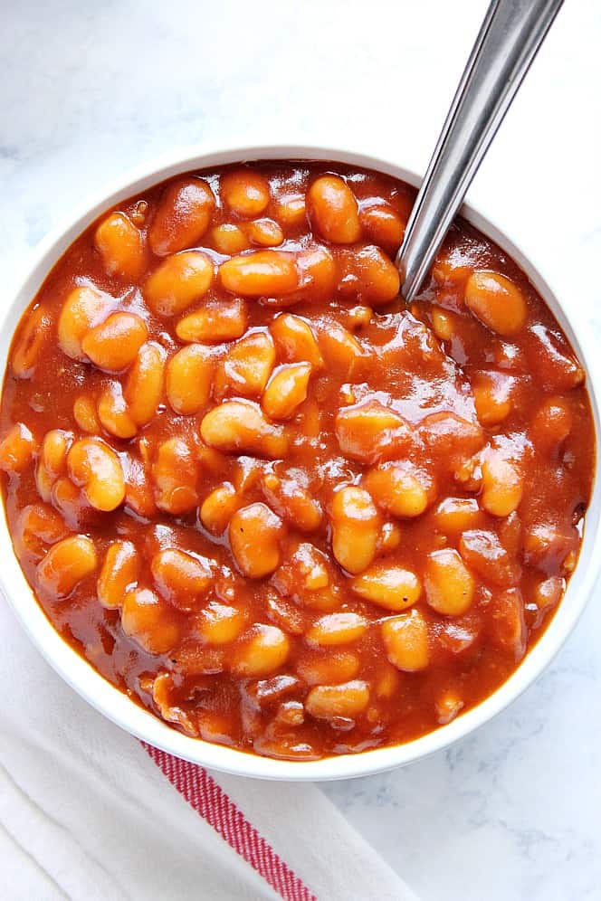 Overhead shot of baked beans in white bowl with spoon.
