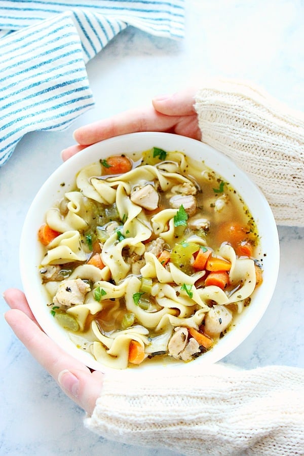 Chicken Noodle Soup in a bowl held with hands.