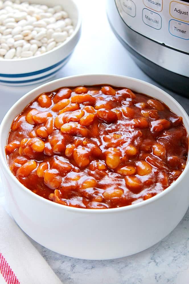 Side shot of baked beans in white bowl with Instant Pot next to it.