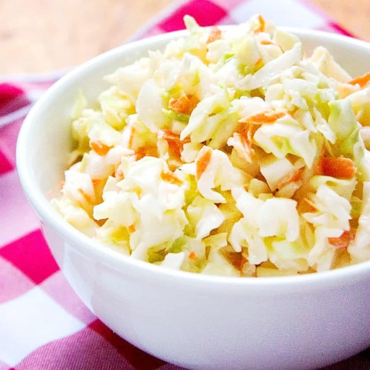 Square image of KFC coleslaw in a white bowl with red plaid napkin.