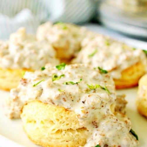 Biscuits on white plate, some covered in gravy.