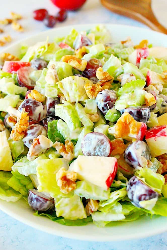 Side shot of Waldorf salad in bowl, wooden salad spoon on side.