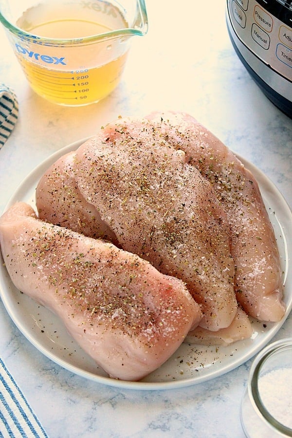 Overhead shot of raw chicken breasts, seasoned, on white plate.