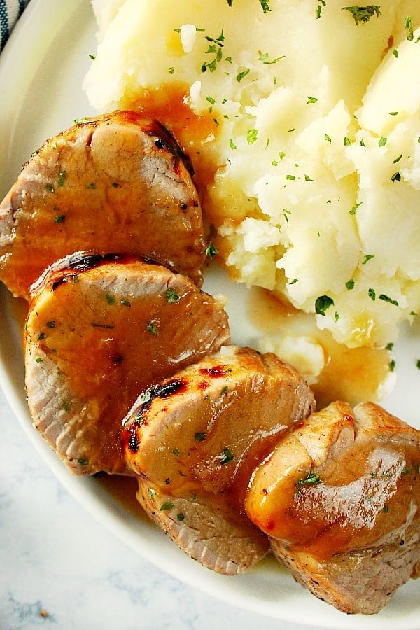 Overhead shot of pork tenderloin slices next to mashed potatoes on plate.