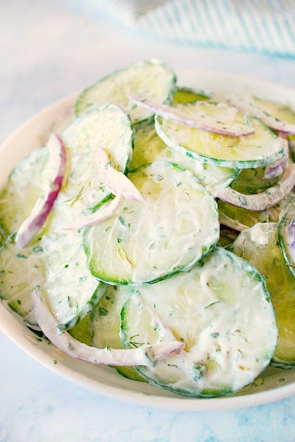 Creamy Cucumber Salad - creamy and refreshing salad with English cucumbers, red onion, garlic, sour cream and parsley or dill. A perfect side dish to grilled meat or as a sandwich topper. Creamy Cucumber Salad in a white salad bowl.