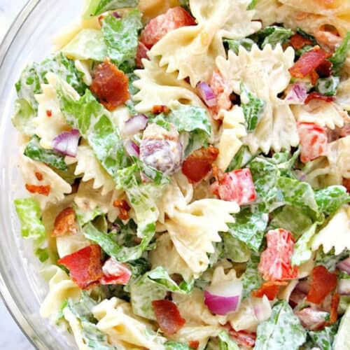 Pasta salad with tomatoes and bacon in a glass serving bowl.