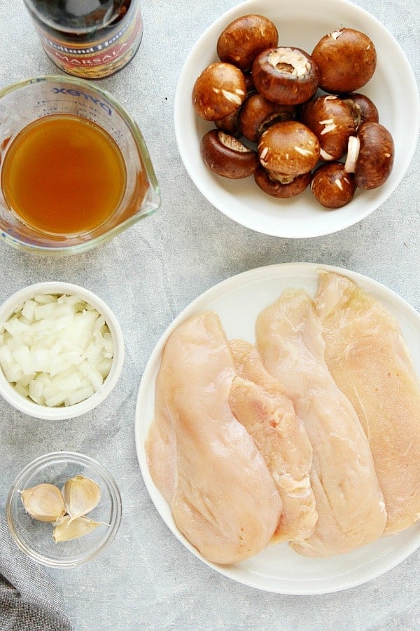 Ingredients for Chicken Marsala dish in bowls, on a gray board.