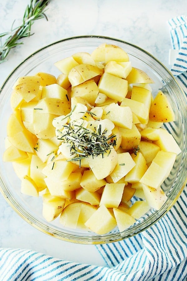 Chopped yellow potatoes with rosemary and garlic in glass bowl.