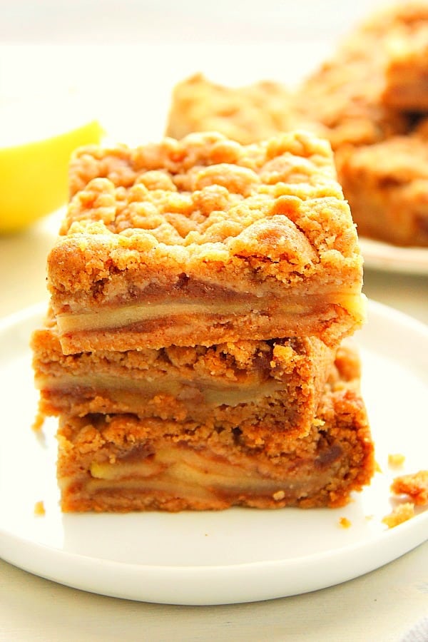 These Easy Apple Pie Bars are a sweet and delicious fall dessert made with apple pie filling layer and cinnamon streusel topping. Apple Pie Bars stacked up on a white plate.