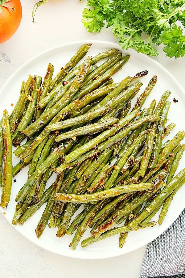 These Roasted Green Beans with garlic and herbs is a quick and delicious side dish idea! They pair perfectly with almost any dish! Roasted Green Beans on white plate.