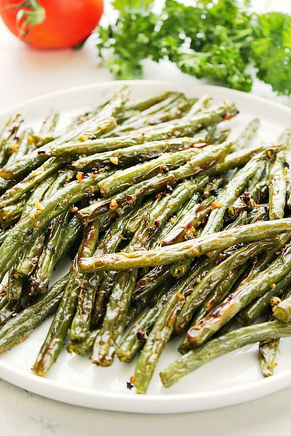 Roasted Green Beans on a plate, next to tomato and parsley.