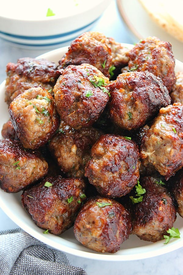 Greek Meatballs aka Keftedes are made with ground lamb (or beef, turkey, etc.) and seasoned to perfection. Greek Meatballs in a white serving bowl.