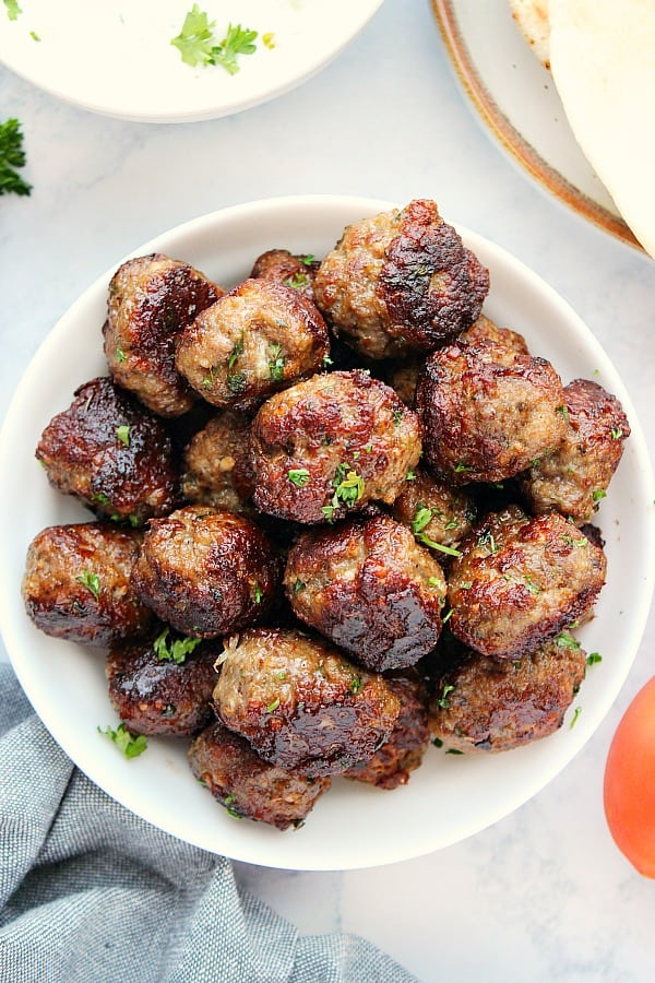 Greek meatballs in a white bowl, next to cucumber garlic sauce.