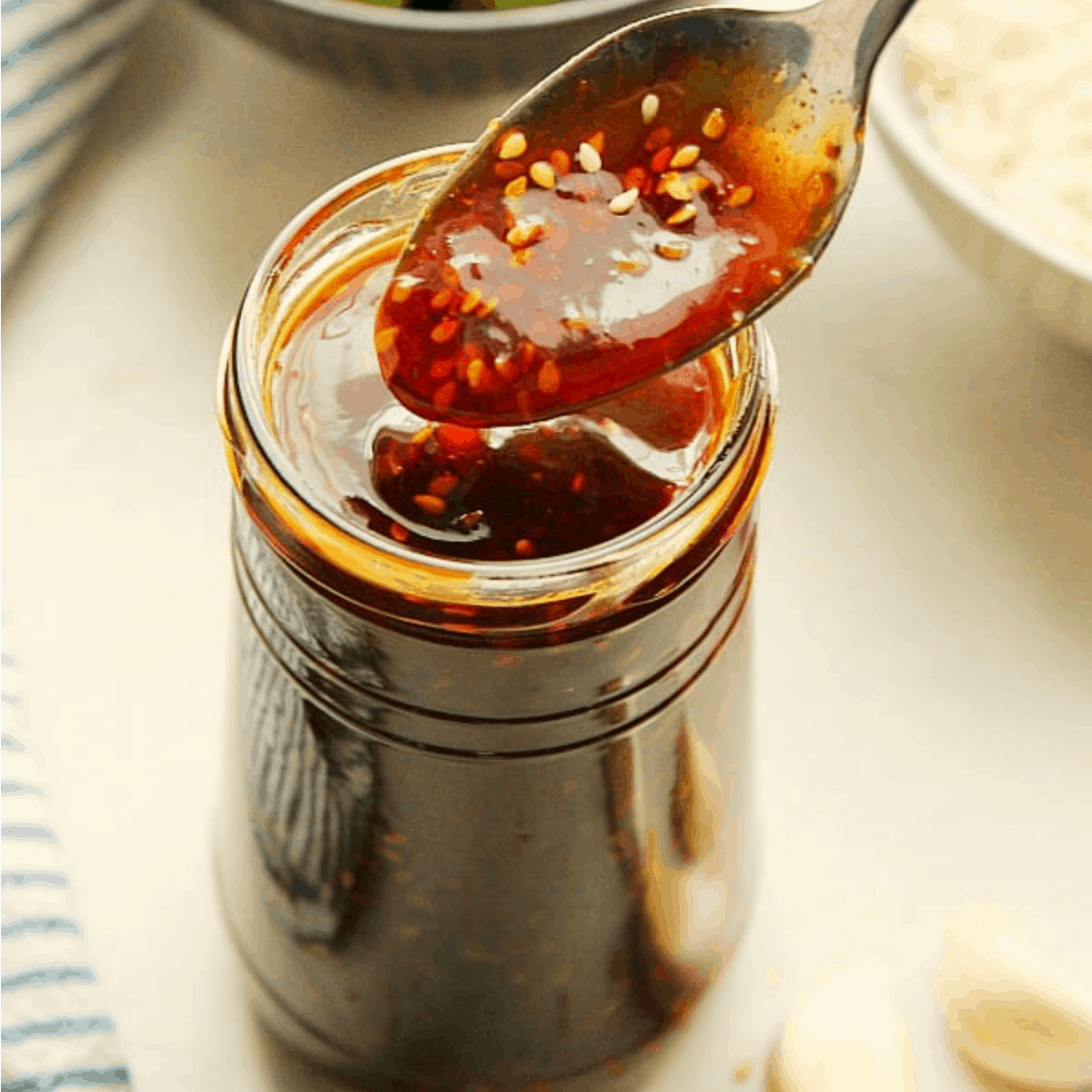 Teriyaki sauce in a jar with spoon drizzling the sauce.