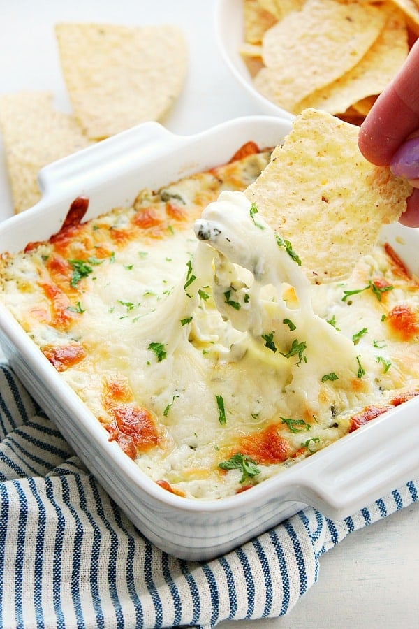 How to make the best Cheesy and Creamy Spinach Artichoke Dip. Spinach Artichoke Dip in a baking dish with chips.