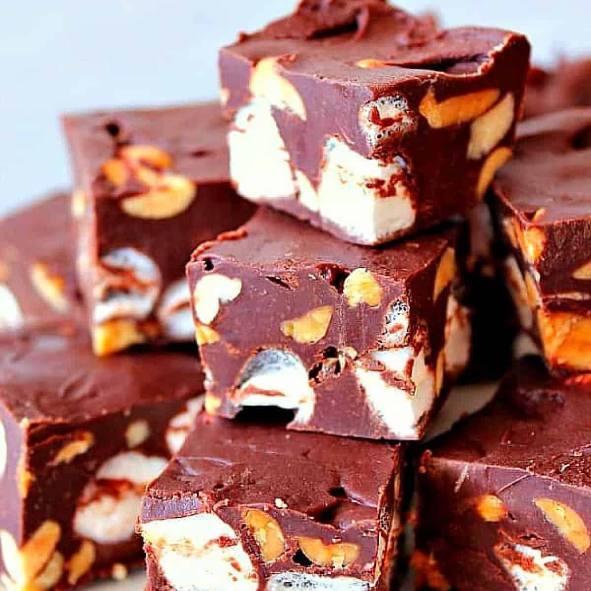 Squares of chocolate fudge with nuts and marshmallows stacked on a plate.